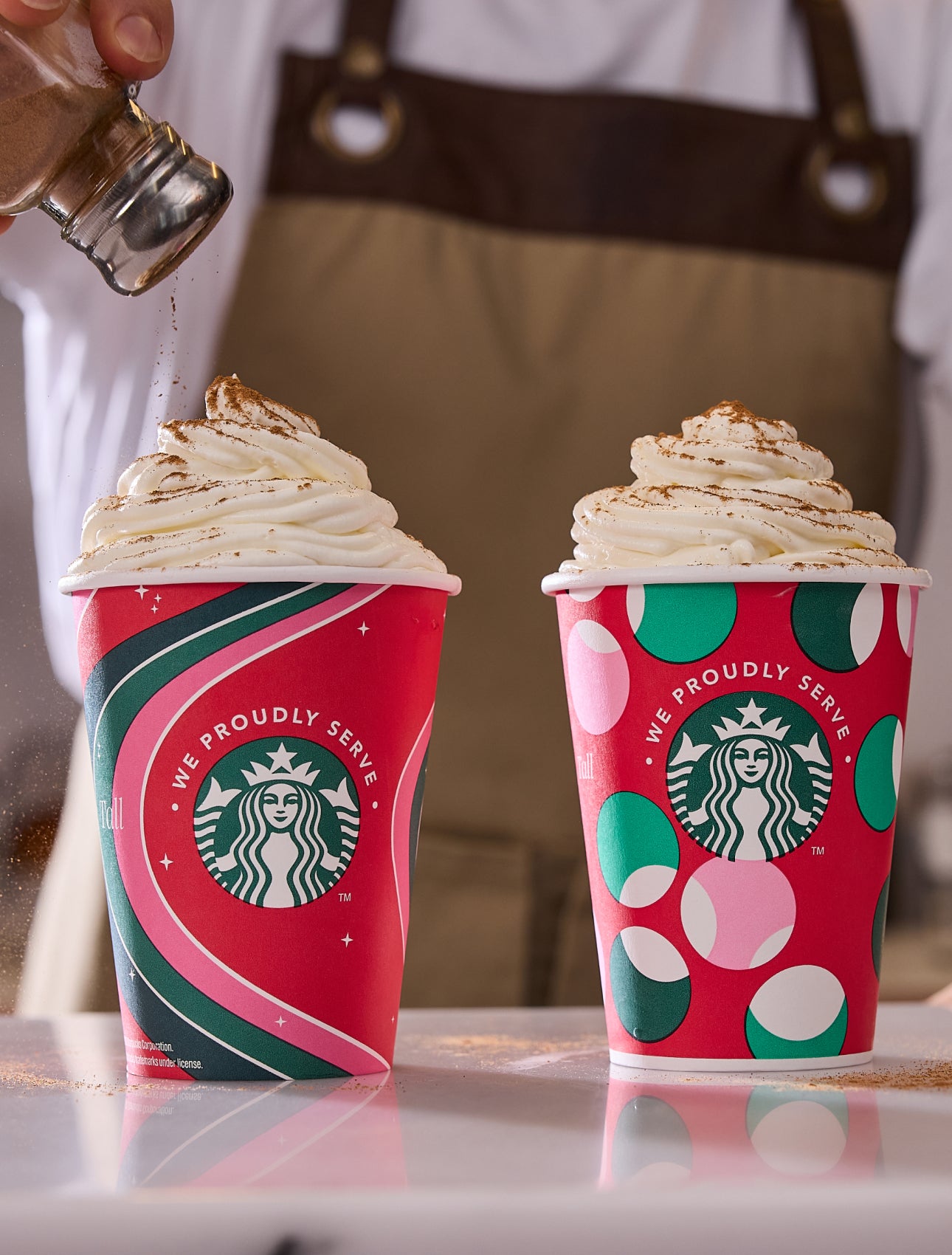Deux boissons frappées Frappuccino® servies dans des tasses festives We Proudly Serve Starbucks, l’une d’elles étant saupoudr
