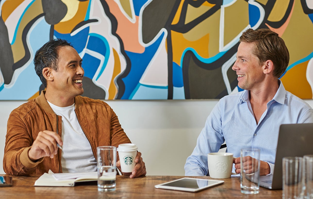 Des hommes assis à une table tenant un café We Proudly Serve Starbucks