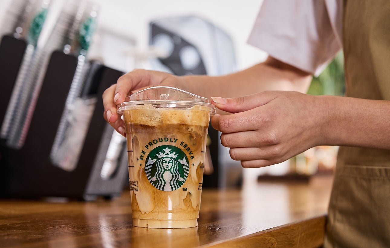 Un barista pose un couvercle sur une tasse de café glacé We Proudly Serve Starbucks, nappée de volutes de crème et de café