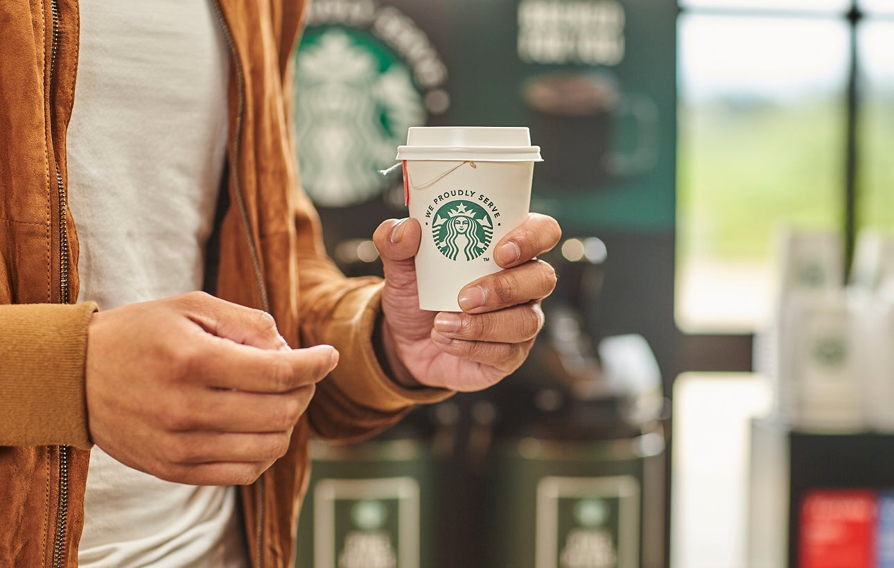 Une personne tenant une tasse de thé dans une tasse portant l’inscription We Proudly Serve Starbucks