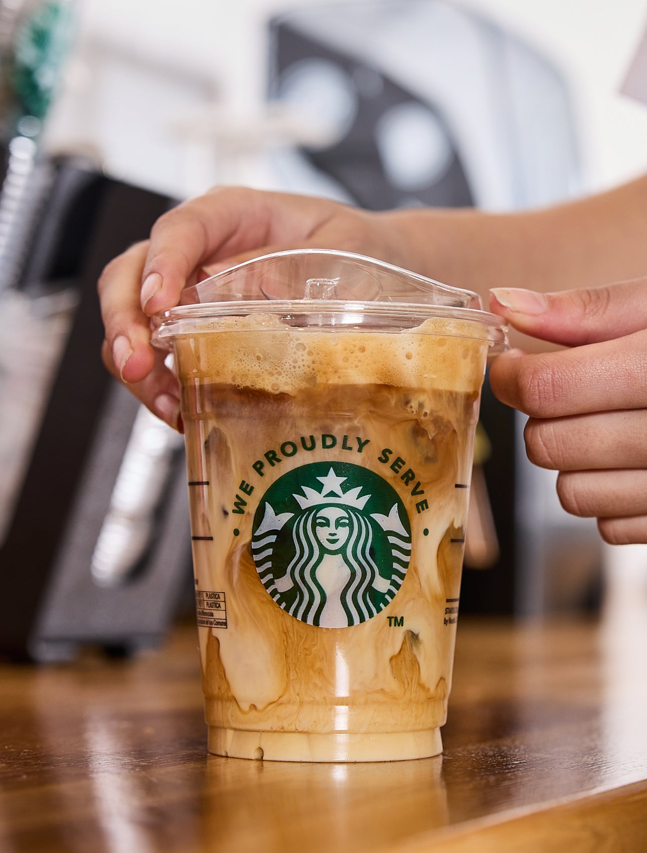 Un barista pose un couvercle sur une tasse de café glacé We Proudly Serve Starbucks, nappée de volutes de crème et de café