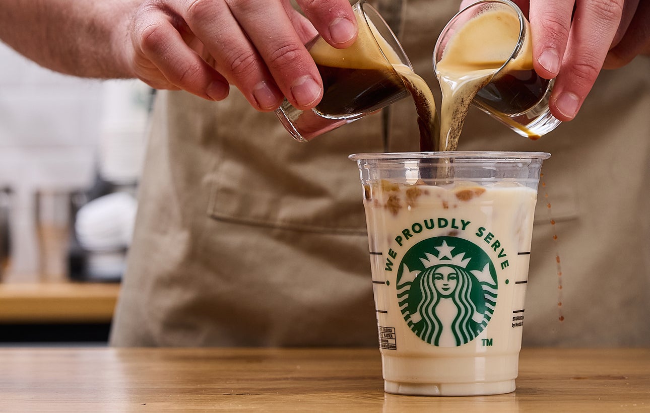 Un barista verse simultanément deux doses d’expresso dans une tasse We Proudly Serve Starbucks remplie de glaçons et de lait 