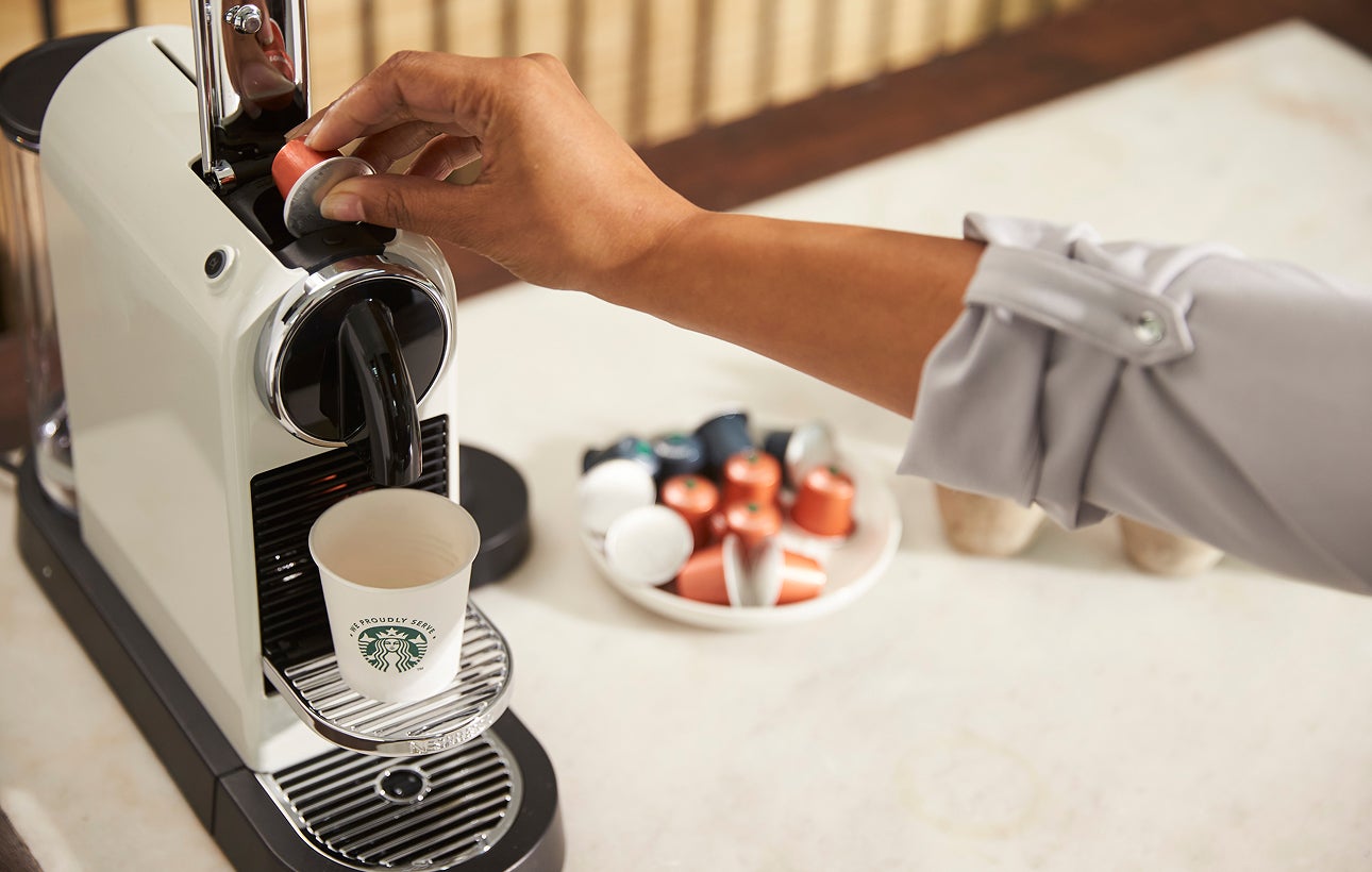 A person sitting down, holding a We Proudly Serve Starbucks takeaway cup with both hands