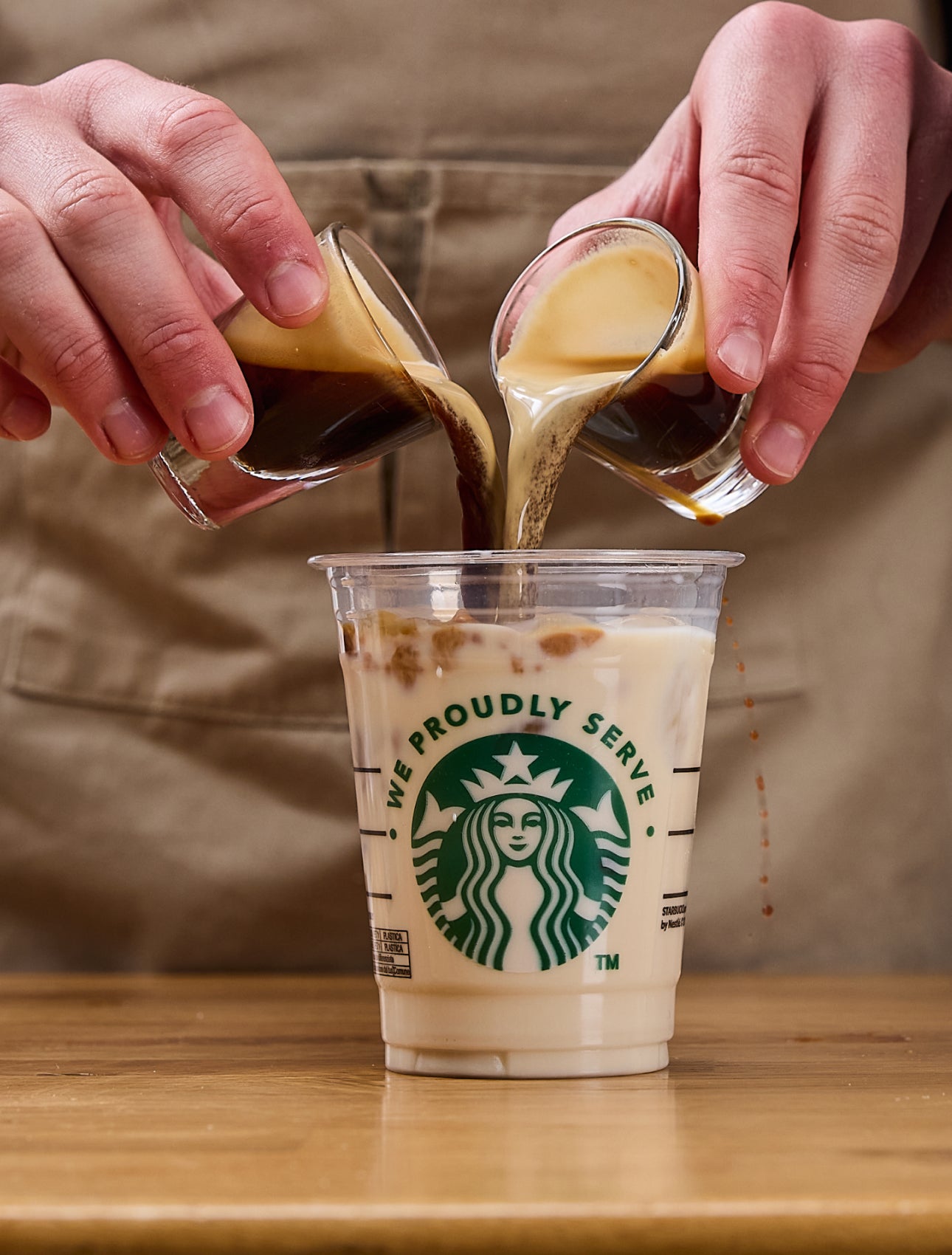 Un barista verse simultanément deux doses d’expresso dans une tasse We Proudly Serve Starbucks remplie de glaçons et de lait 