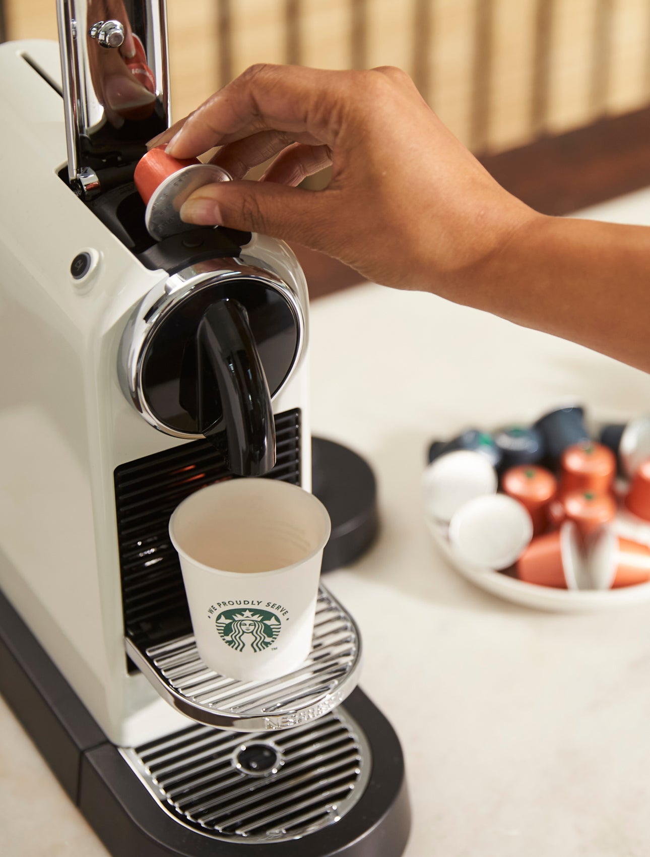 A person sitting down, holding a We Proudly Serve Starbucks takeaway cup with both hands
