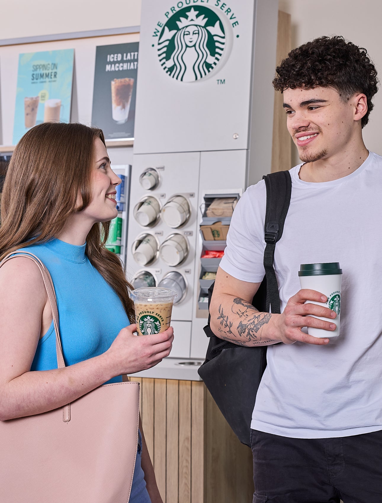 Un homme et une femme debout devant une station à café en libre-service We Proudly Serve Starbucks