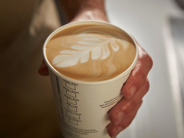 Une main tenant une tasse de café Starbucks We Proudly Serve avec un motif de latte art sur le dessus