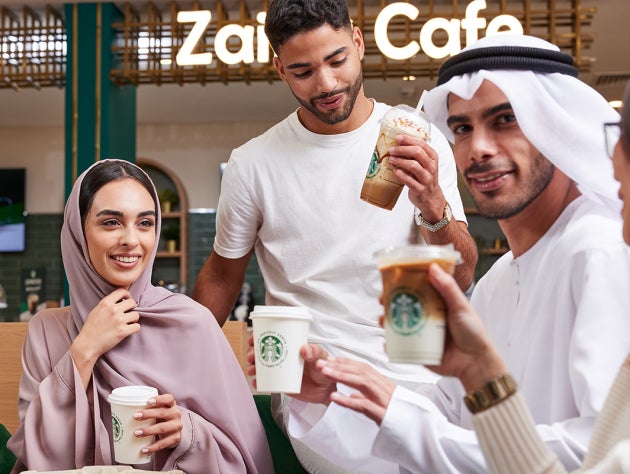 Un groupe d’amis souriants brandit trois boissons glacées Starbucks.