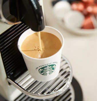 Une tasse We Proudly Serve Starbucks remplie de café préparé sur place à la machine à expresso à portion individuelle