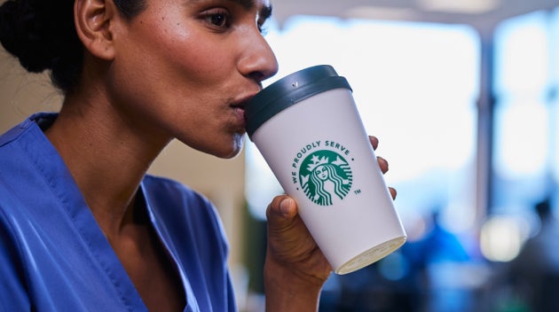 Un travailleur du secteur de la santé en blouse bleue sirotant un café We Proudly Serve Starbucks en étant assis dans un rest