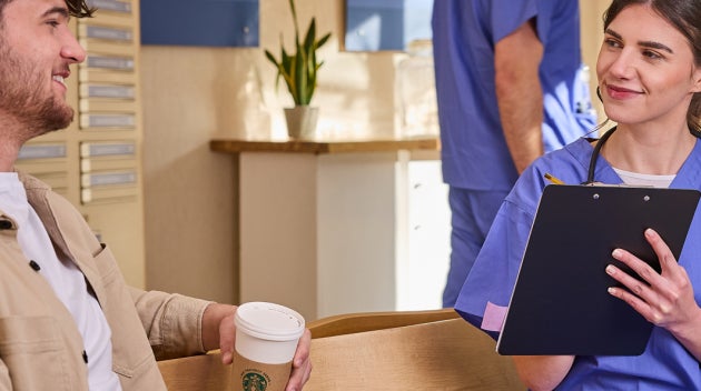 Dans un centre de soins, une femme en blouse bleue parlant à une patiente qui tient une tasse de café We Proudly Serve Starbu